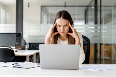 Stresli ve endişeli iş kadını, modern ofis çalışmalarının zorlu ve talepkar yönlerinin bir göstergesi olarak dizüstü bilgisayara bakarak el ele tutuşuyor. İş dünyasının gerçek baskısı.