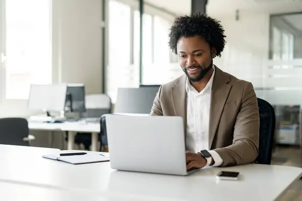 自信に満ちたアフリカ系アメリカ人の実業家が ノートパソコンを使って近代的なオフィスに座っている プロのビジネス環境における戦略的思考の概念 — ストック写真