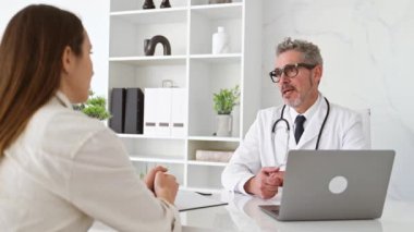 Kıdemli bir doktor, el değmemiş bir klinikteki muayene sırasında genç bir kadın hastayla bir tedavi planını paylaşıyor. Samimi ve güvenilir bir doktor-hasta ilişkisi gösteriyor.