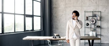 Geniş panoramik bir çekimle yakalanan Brezilyalı genç bir işadamı, doğal ışık ile dolu çağdaş bir ofiste canlı ve nişanlı bir şekilde telefonla konuşuyor.