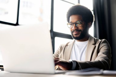 İçerik tebessümü ve dizüstü bilgisayarındaki bakışlarıyla bu Brezilyalı girişimci modern profesyonellerin zevk dengesini ve kendini sanatına adamışlığını parlak bir ofis ortamında somutlaştırıyor..