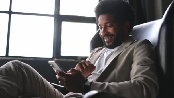 カスタマイズされたスーツの笑顔のビジネスマンは 現代の専門家生活におけるモバイル技術のシームレスな統合を示し スマートフォンで接続の瞬間を楽しんでいます — ストック動画