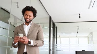 Havadar bir ofis alanında, genç bir Afro-Amerikalı işadamı akıllı telefonuyla etkileşime geçiyor, modern iş dünyasının dijital araçlarını ve bağlantılarını gösteriyor.