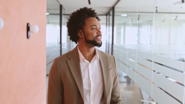 一位年轻 现代的商人带着轻松而自信的举止穿过办公室走廊 他的微笑反映出一种积极的企业氛围 男性企业家准备好工作日 — 图库视频影像