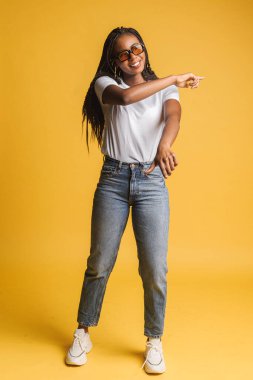 Güneş gözlüklü heyecanlı kadının sarıda izole edilmiş dans edişinin geniş bir görüntüsü. Pembe kazaklı çılgın kadın elini kaldırıyor, ritm tutuyor. Mutluluk ve yaşam tarzı kavramı