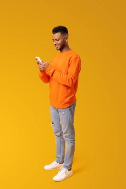 Joyful and carefree man using smartphone isolated on yellow, guy spends leisure in social networks, chatting online, shopping, using new mobile app, full length, vertical