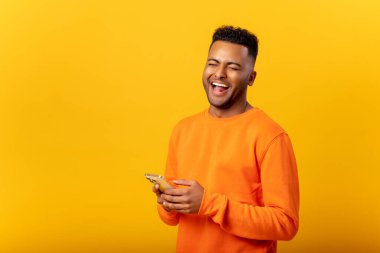 İyimser Hintli adam akıllı telefondan mesaj atıyor ve gülüyor, gülümsüyor sarı renkte izole edilmiş yeni mobil uygulama kullanıyor.