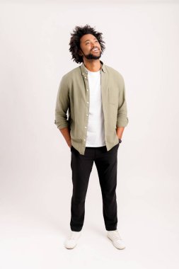 Gömlekli mutlu genç adamın portresi. Kolları ceplerinde duruyor ve dişlek bir gülümsemeyle yukarı bakıyor. Beyaz arka planda çekilen kapalı stüdyo.