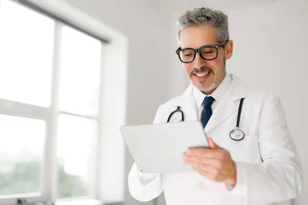 Radosny Starszy Lekarz Siwymi Włosami Okularami Przegląda Informacje Tablecie Demonstrując — Zdjęcie stockowe