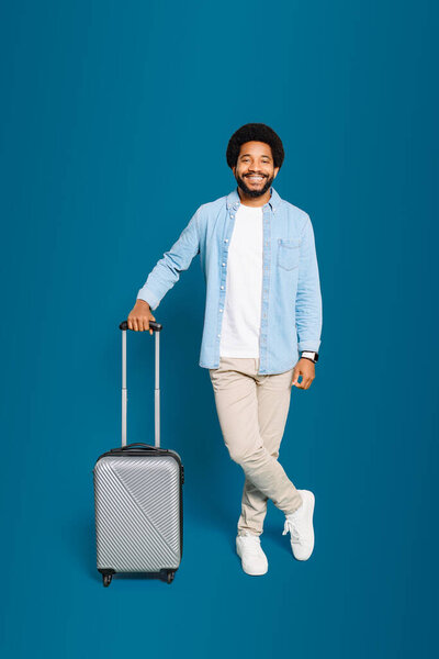 A young man with a bright smile leans casually on his modern suitcase, exuding confidence and the ease of travel. Concept of carefree exploration and the joy of embarking on a new adventure.