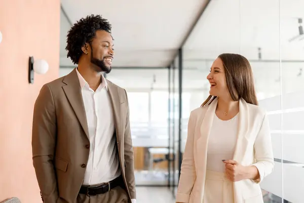 A businesswoman and businessman walk through the office with confidence, their conversation suggesting a shared vision and professional camaraderie. Teamwork concept