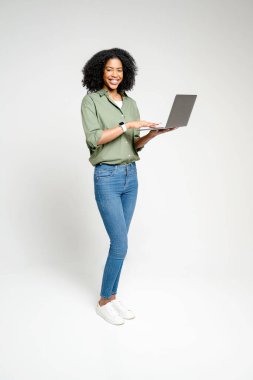 Tam boy çekimde, neşeli bir ifadeyle dizüstü bilgisayar kullanan Afro-Amerikalı bir kadın, hareketlilik ve esneklik sağlayan modern kablosuz cihazların çok yönlülüğünü gösteriyor.