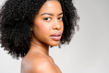 Kafasını çevirir ve kurnaz bir bakışla, Afro-Amerikalı bir kadın sessiz bir güç ve zarif bir güzellik yayar, şehvetli kıvırcık saçları ve sırt dekolteli sütyeninin basitliğiyle tamamlanır.