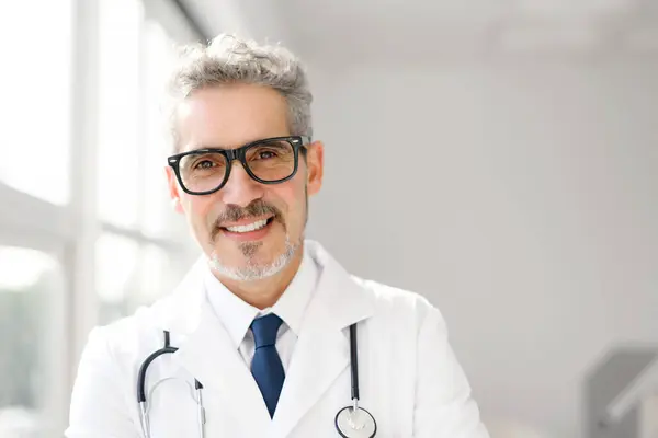在一间明亮的办公室里 一位白发苍苍 戴眼镜的杰出医生自信地站在那里 这意味着他具备应对医疗挑战的能力和准备状态 经验丰富 有信心的资深医生 — 图库照片