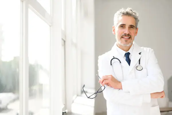 Senior Doctor Stands Confidently Sunlit Clinic His Arms Crossed While — Stock Photo, Image
