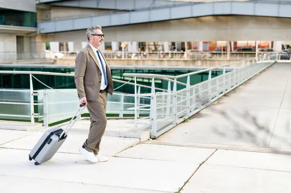 成熟した灰色の髪のビジネスマン スーツケースと先を見るために 常に外出中のプロのダイナミズムを示しています 旅行とビジネスコンセプト — ストック写真