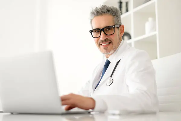 Senior Doctor Grey Hair Looks Camera While Using Laptop Suggesting Stock Picture