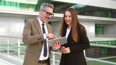 Dijital tablet kullanan ve ayakta duran iki farklı iş arkadaşı, genç bir bayan çalışana koçluk yapan ya da özel ders veren gri saçlı bir iş adamı, konuşuyorlar ve tartışıyorlar.