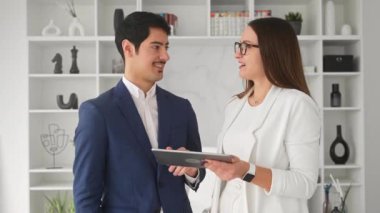 Dost canlısı bir İspanyol işadamı, kadın meslektaşı ile parlak, modern bir ofiste bir tablet üzerinde tartışır. Etkili bir iletişim ve olumlu bir iş ilişkisi önerir.