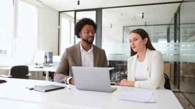 İki iş arkadaşı, bilgisayar kullanarak ve görevleri birlikte çözerek, şirket ortamında takım çalışması ve işbirliğini işaret eden evrak işleriyle ilgili yapıcı bir tartışmaya giriştiler.