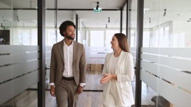 Modern bir ofis koridorunda, bir Afro-Amerikalı işadamı ve meslektaşı canlı bir tartışma içindeler, birlikte yürüyorlar, bir akıl hocalığı veya iş birliği kavramını yansıtıyorlar..