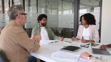 Meslektaşlar bir dizüstü bilgisayarın etrafında sohbet ederken, bir üye bir konsepti açıklarken, takımların dikkati ve açık vücut dili işbirlikçi ve algılayıcı bir çalışma ortamı göstermektedir.