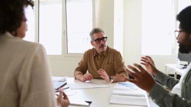 Ofis tartışması sırasında meslektaşını dikkatle dinleyen tişörtlü, olgun, gri saçlı profesyonel bir adam destekleyici ve yapıcı bir iş diyaloğunu ve dostane bir atmosferi temsil ediyor.