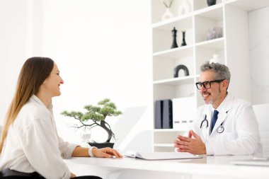 Üst düzey bir doktor, el değmemiş bir klinikteki muayene sırasında genç bir hastayla gülüşüp samimi ve güvenilir bir doktor-hasta ilişkisi sergiliyor.