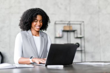 Profesyonel bir Afro-Amerikalı kadın dizüstü bilgisayarına odaklanmış, ifadesini ciddi ve konsantre bir şekilde modern bir iş kadınının ithafını somutlaştırıyor..