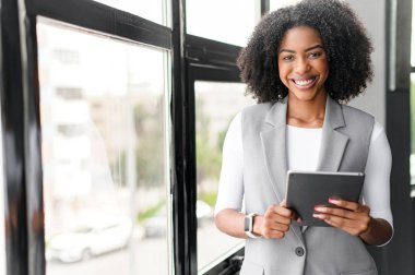 Çekici bir Afro-Amerikalı iş kadını ofisinde tablet kullanıyor, günümüzde dijital iş dünyasında adaptasyon ve teknoloji zevkini gösteriyor..