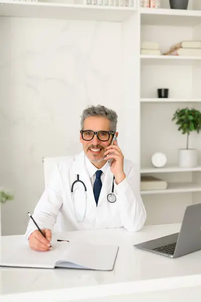 stock image A seasoned medical professional is engaged in writing medical records, showcasing his dedication to patient care and attention to detail in a contemporary clinic setting.