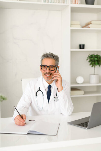 A seasoned medical professional is engaged in writing medical records, showcasing his dedication to patient care and attention to detail in a contemporary clinic setting.