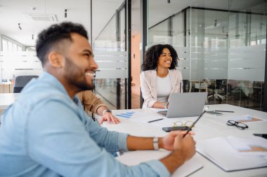 Modern ofis ortamındaki çeşitli bir ekip verimli bir iş toplantısı yaptı. Gülümseyen profesyoneller dizüstü bilgisayarlar ve belgeler üzerinde çalışırken stratejilerini tartıştılar, takım çalışmalarını ve işbirliğini teşvik ettiler.