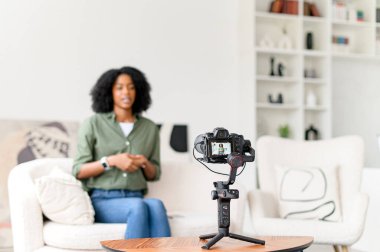Afro-Amerikalı bir kadın eğitim videosu çekmeye hazırlanıyor. Minimalist ama davetkar oturma odasında kameranın önünde rahatça oturuyor..