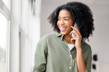 Samimi bir anda, mutluluktan parlayan Afro-Amerikalı bir kadın, akıllı telefonunu kullanır, çekici gülüşü eğlenceli bir sohbete veya heyecan verici bir habere işaret eder..