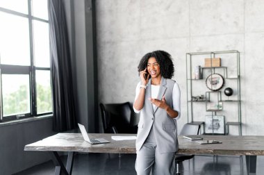 Neşeli bir Afro-Amerikalı iş kadını, neşeli bir telefon konuşması yapmayı seviyor. Keyifli bir profesyonel etkileşime işaret eden neşeli bir jesti ve neşeli bir ifadesi var.