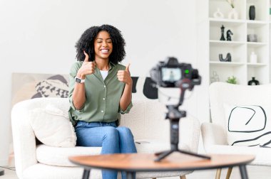 Hevesli bir Afro-Amerikalı kadın motivasyon vlog 'u kaydederken başparmağını kaldırıyor, çekici gülüşü ve etkileşimli oturumunu vurgulayan olumlu hareketi