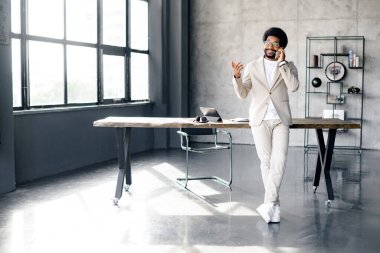 Bu genç iş adamının neşeli tavırları ve şık bej takım elbisesi modern ofis ortamında gevşek kurumsal kültürün yeni bir çağını yansıtıyor.