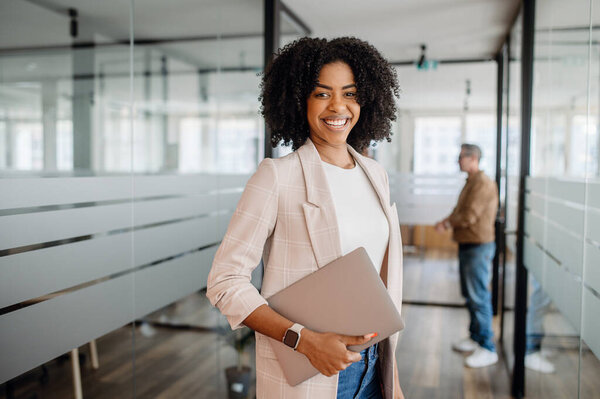 Confident businesswoman standing in a modern office with a laptop, symbolizing leadership, professionalism, and career success in a dynamic corporate environment.