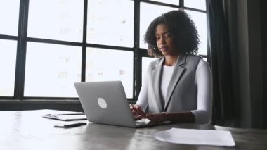Profesyonel Afro-Amerikalı kadın dizüstü bilgisayarına odaklanmış durumda. İfadesi ciddi ve konsantre. Modern bir iş kadınının adanmışlığını simgeliyor..