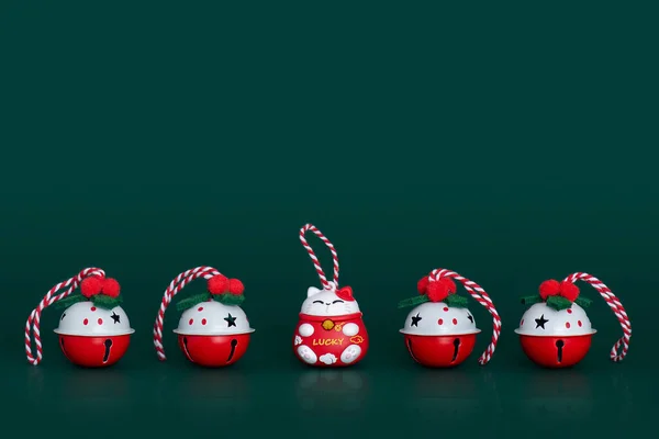 Christmas bells and Lucky cat figure in a row on green background. Christmas theme. Four beautiful red-white decorating jingle bells with swirl ribbons and red-white Lucky cat between them.