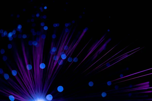 Luminous optical fiber. Fantastic backdrop of illuminated neon purple fiber optic lines and glowing blue bokeh on black. Light guides create a circle with colorful light points in the dark.