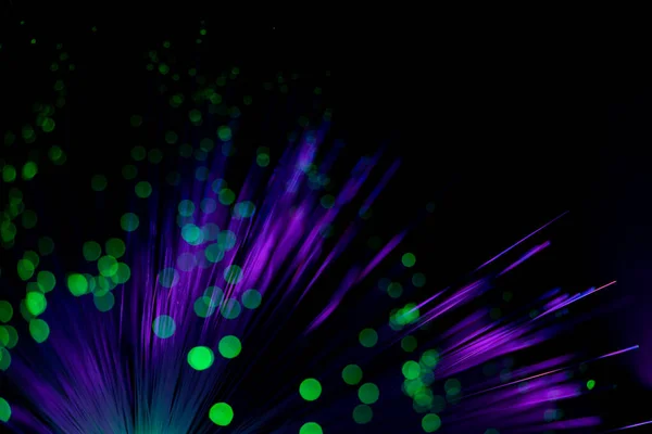 Luminous optical fiber. Fantastic backdrop of illuminated neon purple fiber optic lines and glowing green bokeh on black. Light guides create circles with colorful light points in the dark. Futuristic