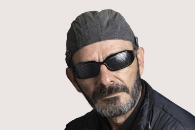 Beyaz arka planda siyah şapkalı, güneş gözlüklü ve sakallı bir adam.