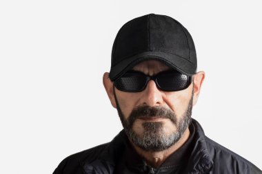 Beyaz arka planda siyah şapkalı, güneş gözlüklü ve sakallı bir adam.