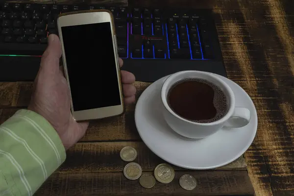 Taza de caf con telfono inteligente y teclado sobre mesa de madera.