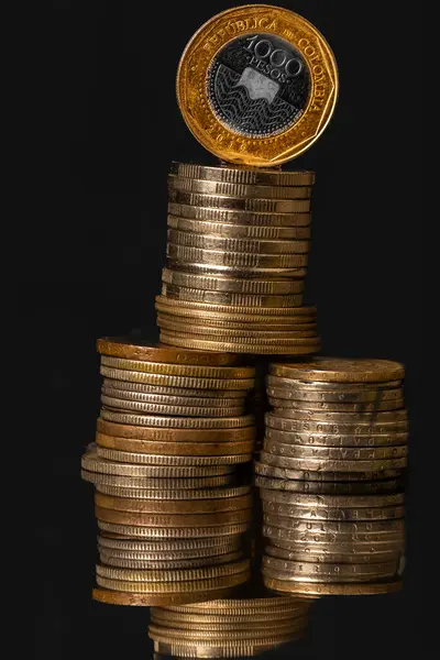 Gold coins and Colombian money on black background: investment and finance business concept.\