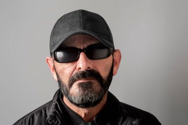 Sakallı, kışlık ceket ve beyzbol şapkası takan yetişkin bir adam..