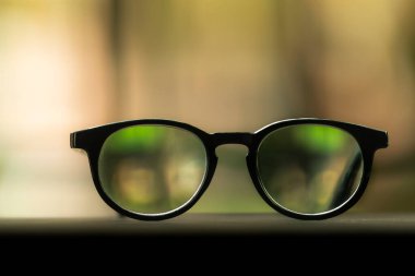 Görsel konsept: Bokeh ile bulanık yeşil bahçe arka planında siyah gözlük