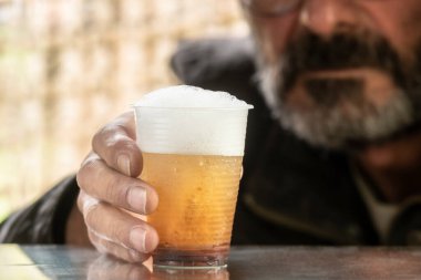 Kirli tırnakları olan, tırnaklarını kaldırmış, arka planda bir bardak bira tutan yalnız sarhoş bir adamın elleri.